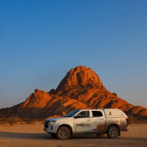 Vehículo 4x4 en el desierto de Namibia frente a una formación rocosa iluminada al atardecer